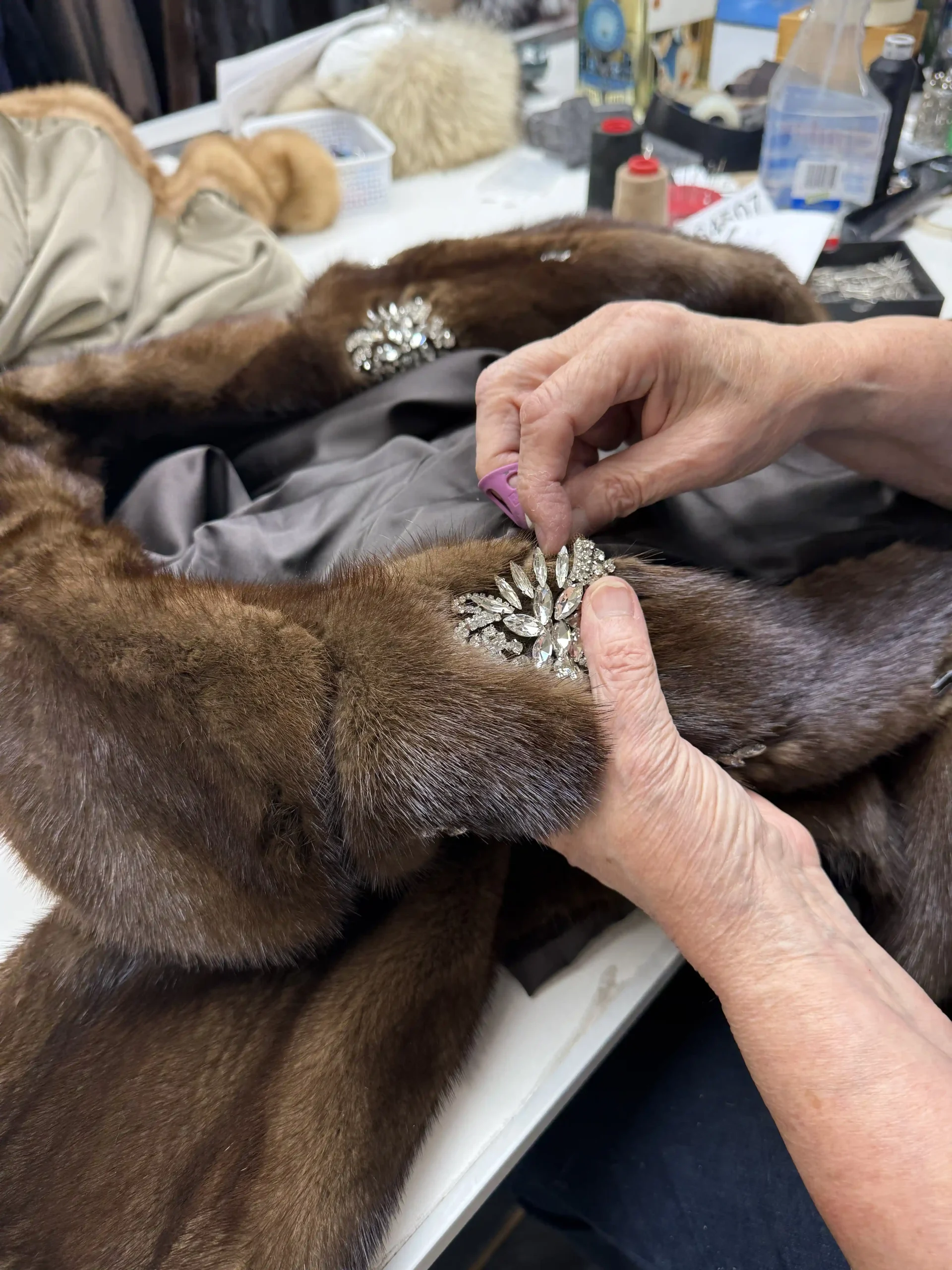 Hands working on a brown fur coat at a workshop table